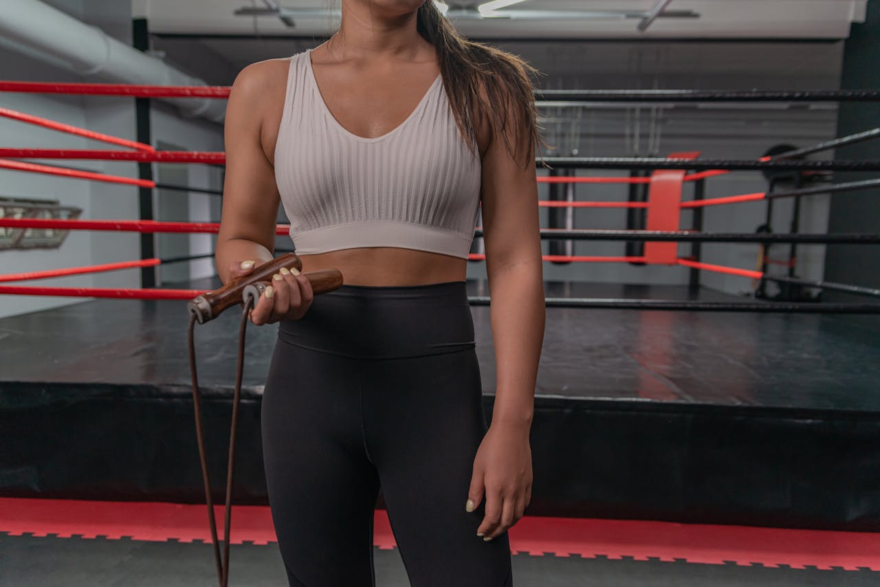 Fit woman holding a jump rope, ready for workout in a boxing gym setting.